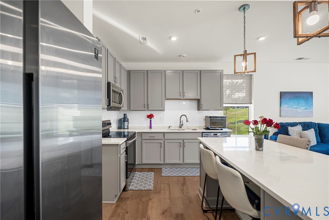 Kitchen featuring grey cabinetry, quartz countertops, stainless steel appliances, wood-finish flooring, and pendant lighting