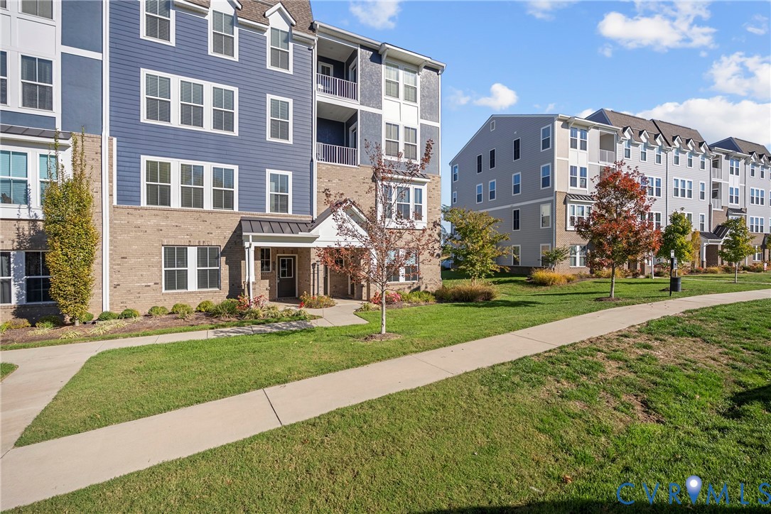 Multi-story building exterior featuring a mix of brick and horizontal siding, private recessed balconies, and paved pedestrian walkways throughout the landscaped grounds