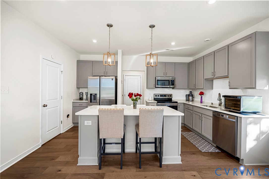 Kitchen featuring grey shaker-style cabinetry, quartz countertops, central island, stainless steel appliances, and wood-finish flooring