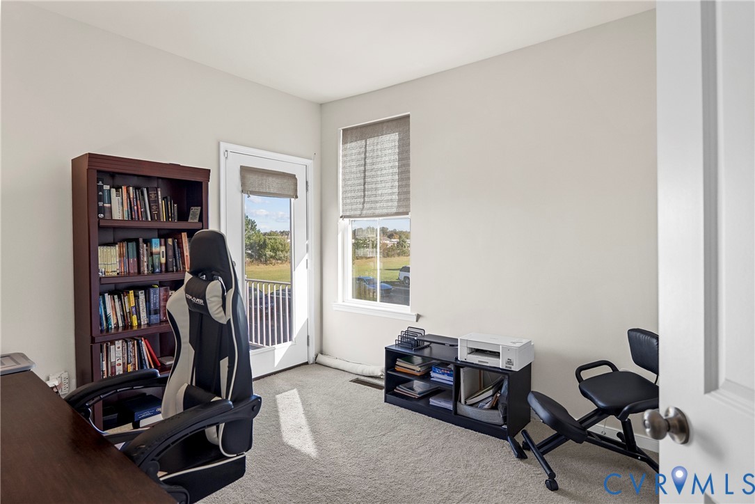 Interior room featuring neutral-toned carpeting, a full-length glass-paneled door, and a single-hung window with a fabric roller shade