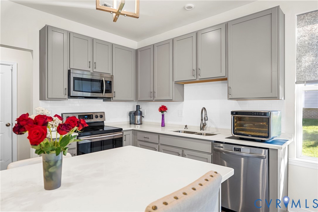 Kitchen featuring gray cabinetry, solid surface countertops, stainless steel appliances, subway tile backsplash, and a center island