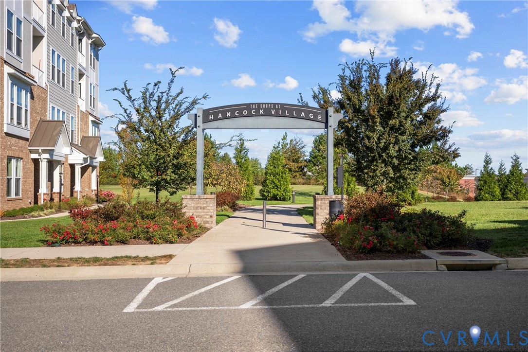 Community entrance featuring masonry signage, concrete pathways, manicured landscaping, and mature trees