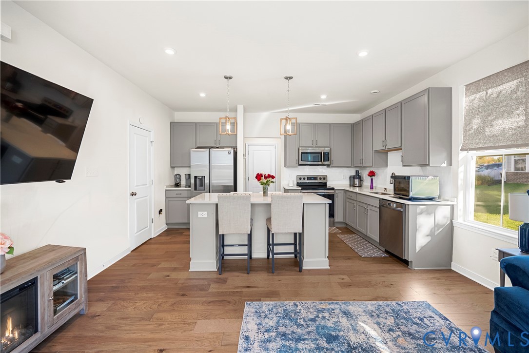 Kitchen featuring grey cabinetry, quartz countertops, a central island, wood-finish flooring, and stainless steel appliances