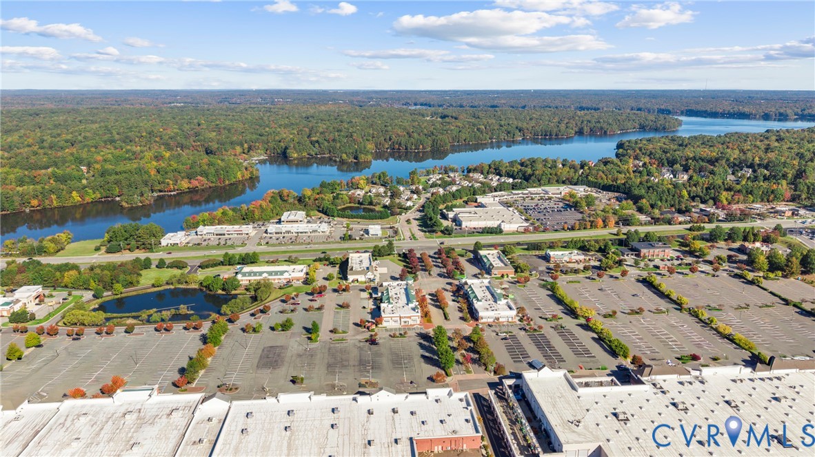 Aerial perspective featuring expansive paved parking surfaces, multiple commercial buildings with flat roofing, and proximity to wooded waterfront areas