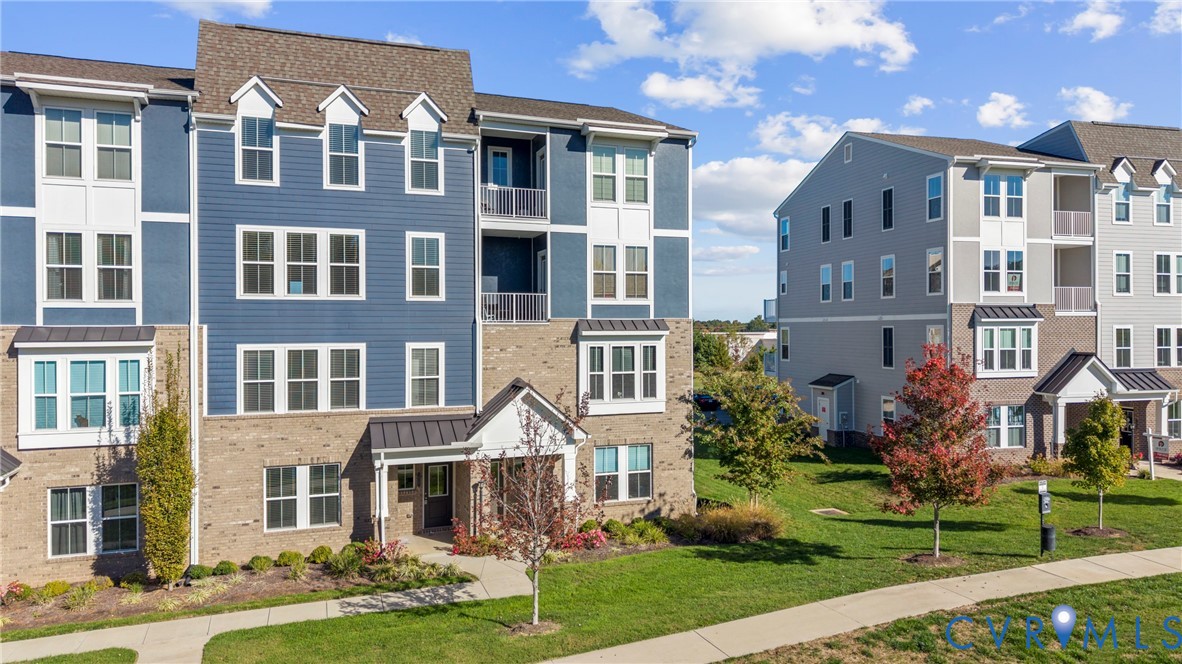 Multi-story building exterior featuring a mix of horizontal lap siding and brick masonry, metal roof accents, recessed private balconies, and multi-pane windows