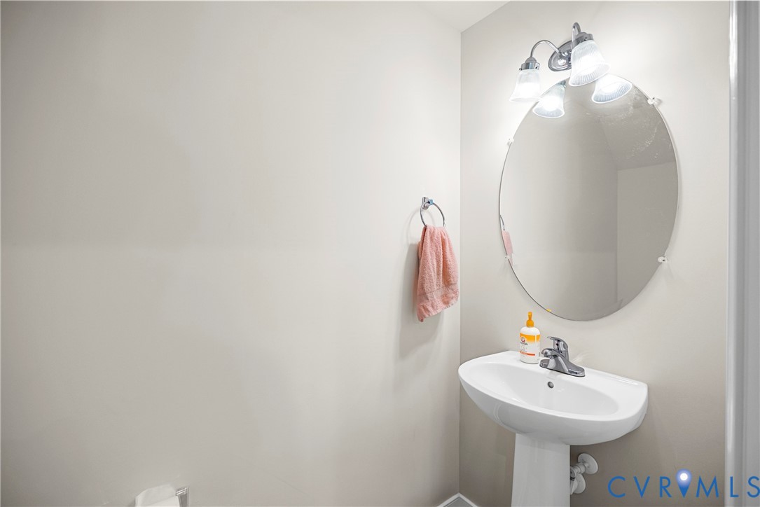 Oval wall-mounted mirror, pedestal sink with chrome faucet, and three-light vanity fixture