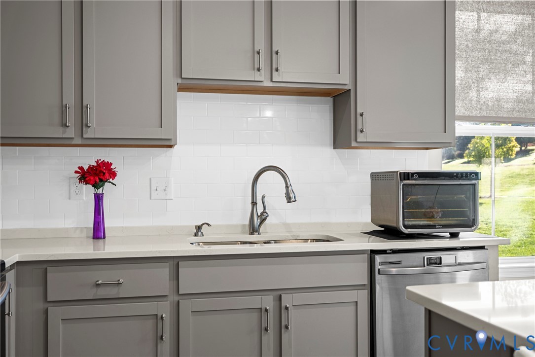 Kitchen featuring gray shaker-style cabinetry, white subway tile backsplash, quartz countertops, undermount stainless steel double-basin sink, and high-arch pull-down faucet