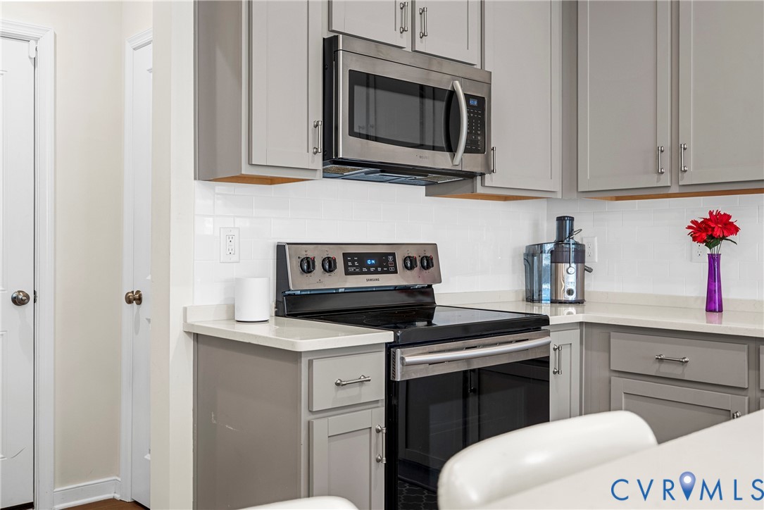 Shaker-style cabinetry with neutral finish, white subway tile backsplash, solid-surface countertops, and stainless steel built-in microwave and range