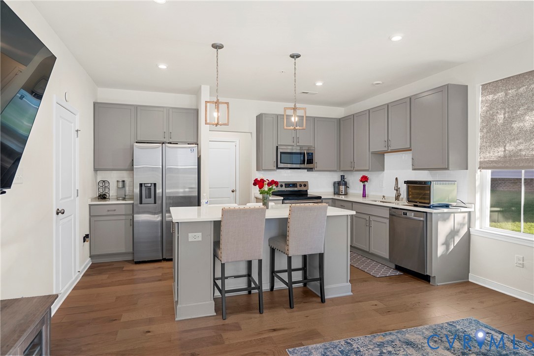 Kitchen featuring grey cabinetry, quartz countertops, a central island with dual pendant lighting, stainless steel appliances, and wood-finish flooring