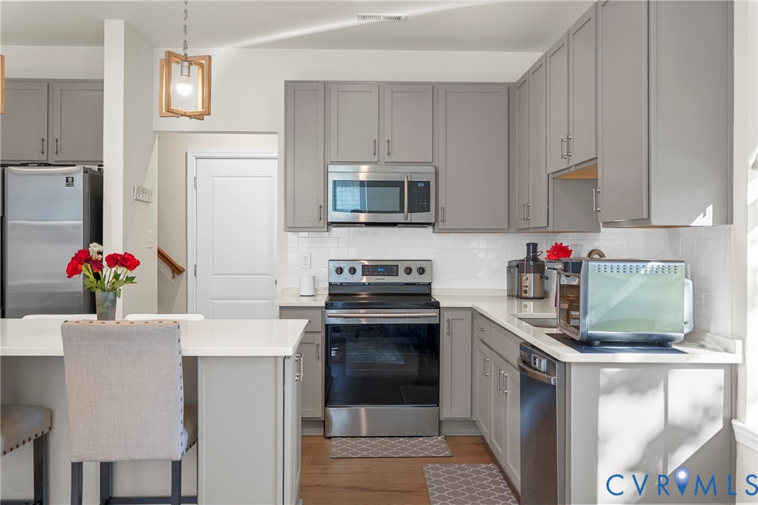 Kitchen featuring shaker-style cabinetry, quartz countertops, subway tile backsplash, stainless steel appliances, and a geometric pendant light