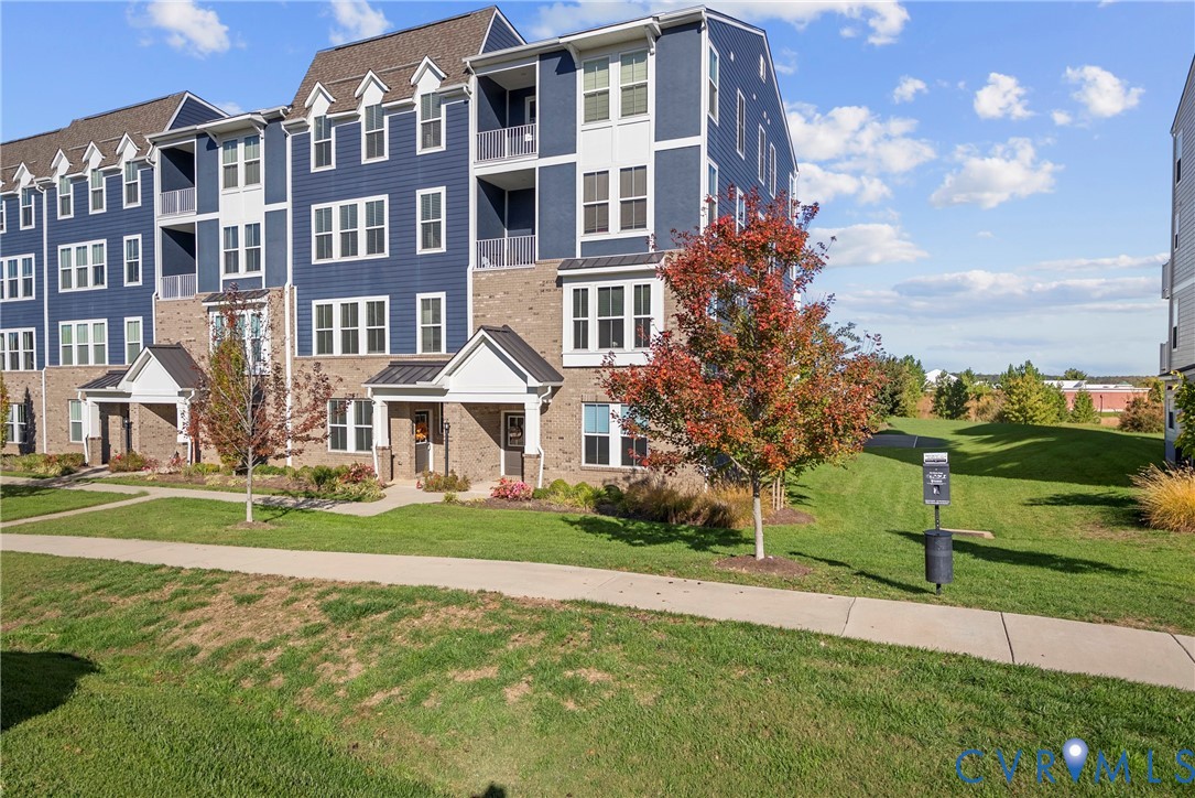 Multi-level exterior featuring dark blue horizontal siding, tan brick masonry, metal-accented gabled roof lines, and private recessed balconies