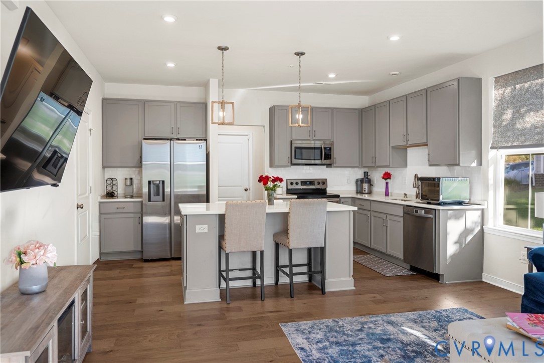 Kitchen featuring light gray cabinetry, a central island with a white countertop, wood-finish flooring, stainless steel appliances, and pendant lighting