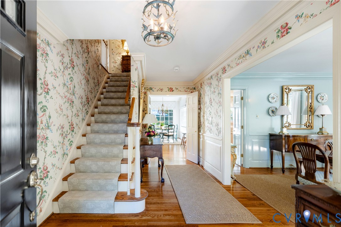The entry foyer features a hardwood floor, wainscoting, crown moulding, a decorative lantern-style chandelier, and stairs with runner to the second floor.