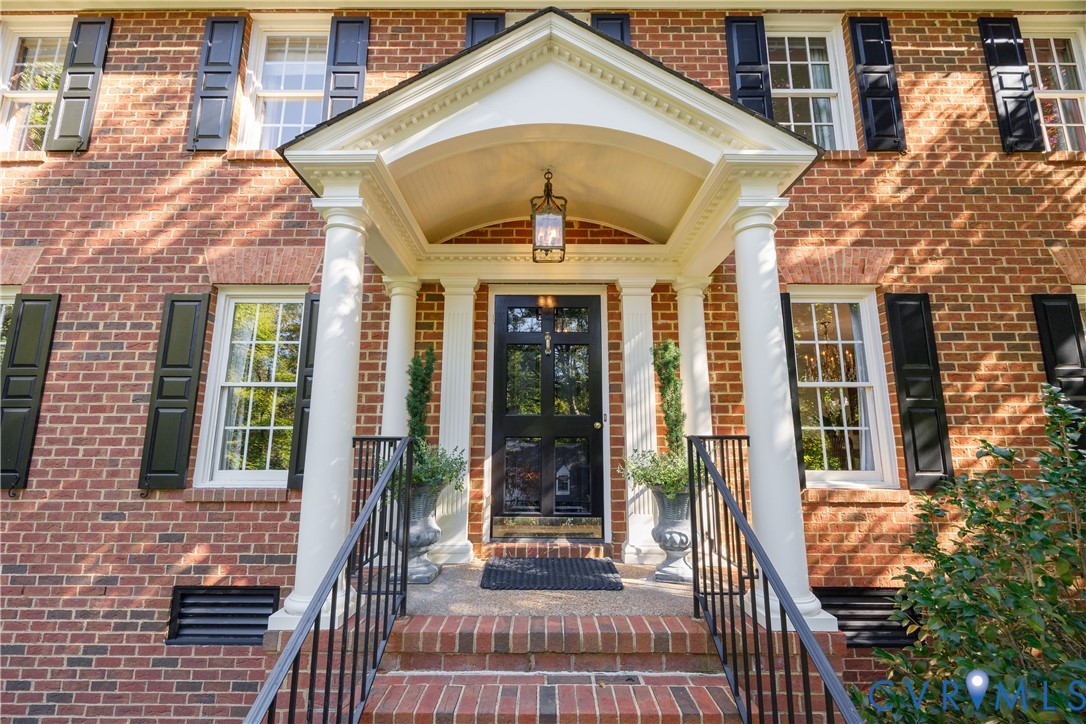 The front entry feaures a classical pedimented portico, dual white columns, a multi-pane front door, and symmetrical dark shutters