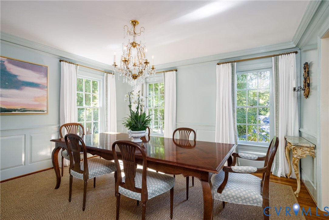 The recently refreshed formal dining room features handsome wainscoting, windows with beautiful views, crown moulding, and a tiered crystal chandelier