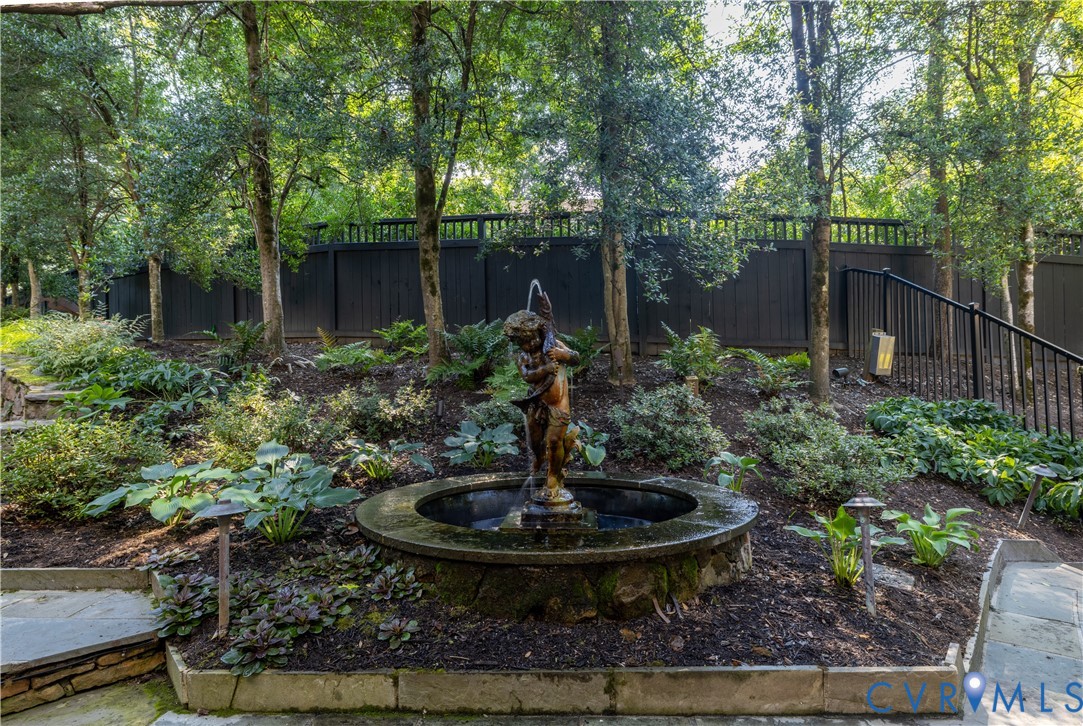 Rear entrance to the landscaped garden features a tiered stone fountain, mature trees, tiered stone retaining walls, and fencing around the entire rear yard.