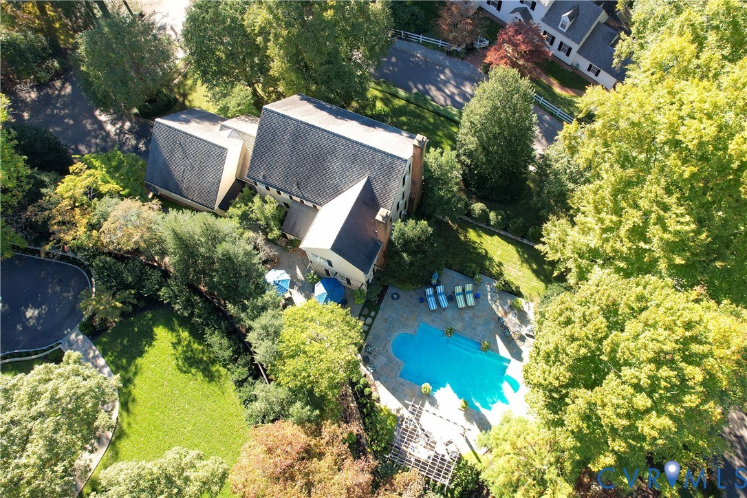 Aerial perspective featuring a multi-story residence with a pitched roof, in-ground swimming pool, stone-surfaced patio, pergola, and landscaped grounds with mature trees
