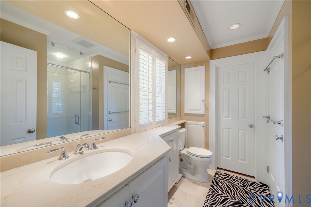 Shared bath between bedrooms two and three features a stone-surface vanity with an integrated oval sink, full-width wall mirror, recessed lighting, white cabinets glass enclosed shower and wall-up access to the third floor. bonus room.