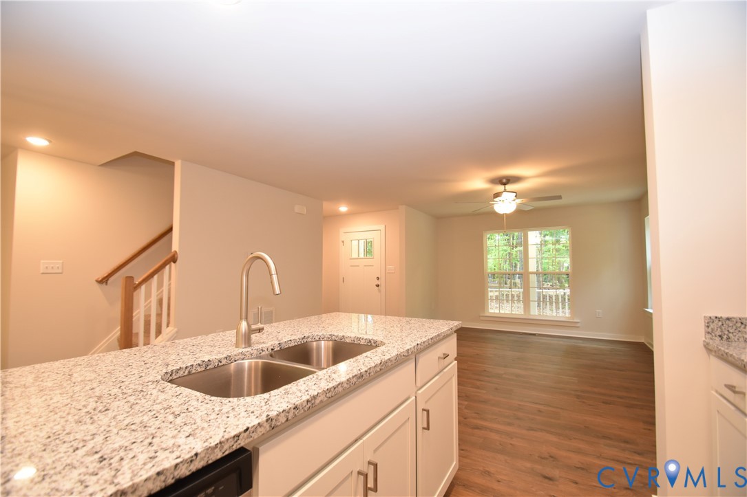 Kitchen island featuring a high-contrast stone countertop, double-basin stainless steel sink, and gooseneck faucet, paired with wood-finish flooring and staircase with wooden handrail Kitchen island featuring a high-contrast stone countertop, double-basin stainless steel sink, and gooseneck faucet, paired with wood-finish flooring and staircase with wooden handrail