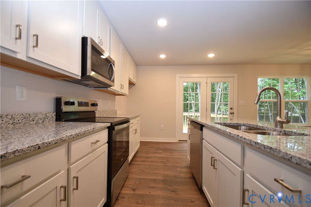 Kitchen featuring white shaker-style cabinetry, stone-finish countertops, stainless steel appliances, recessed lighting, and wood-finish flooring Kitchen featuring white shaker-style cabinetry, stone-finish countertops, stainless steel appliances, recessed lighting, and wood-finish flooring