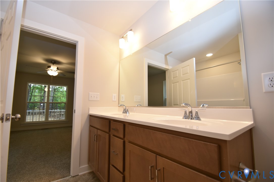 Dual-sink vanity featuring a light-toned solid surface countertop, wood-finish cabinetry, and a full-width wall mirror with integrated vanity lighting