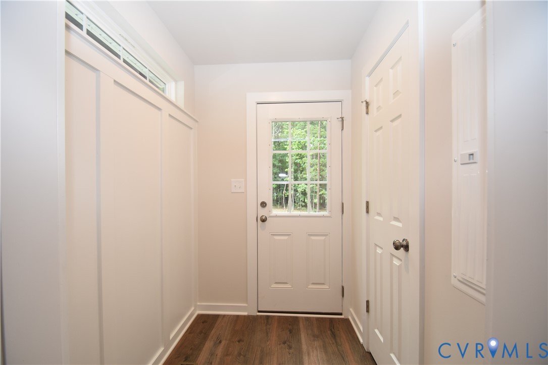 Entryway featuring wood-finish flooring, white board-and-batten wall detailing, a transom window, and an exterior door with glass pane inserts