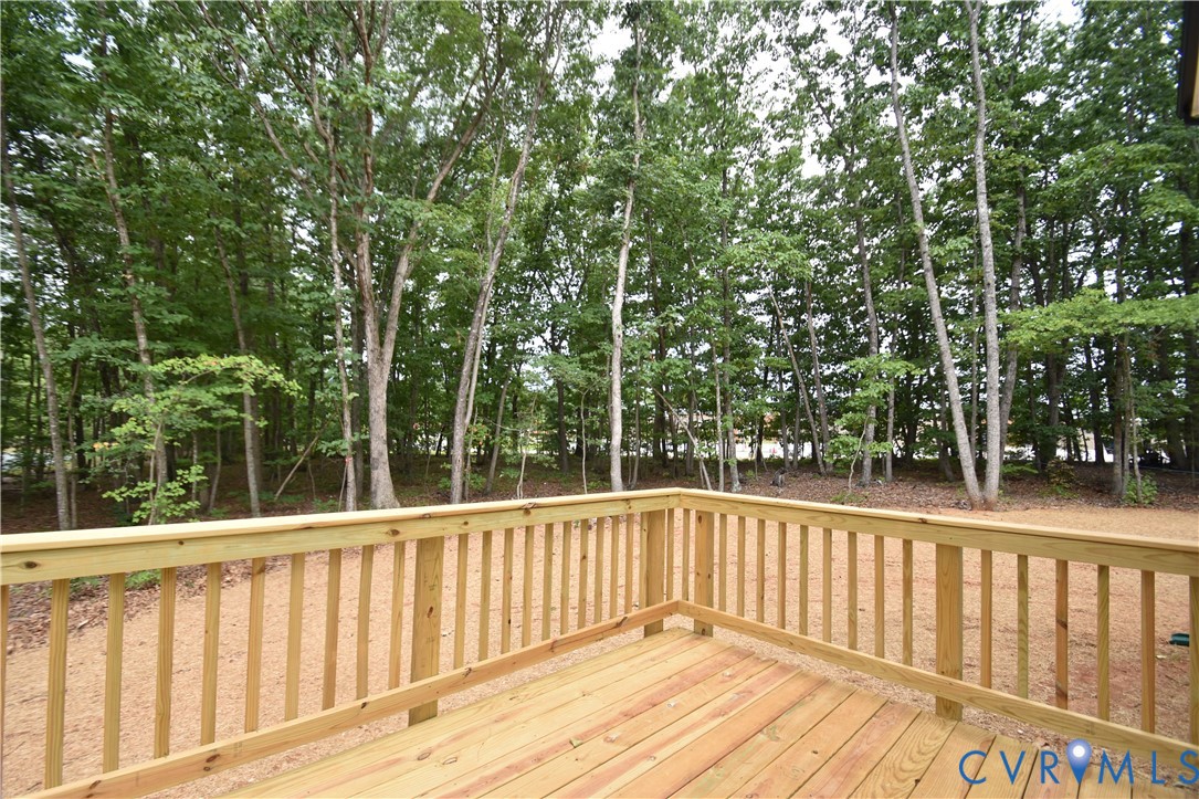 Wood deck featuring a natural finish and vertical balustrade railing, overlooking a wooded lot with mature trees
