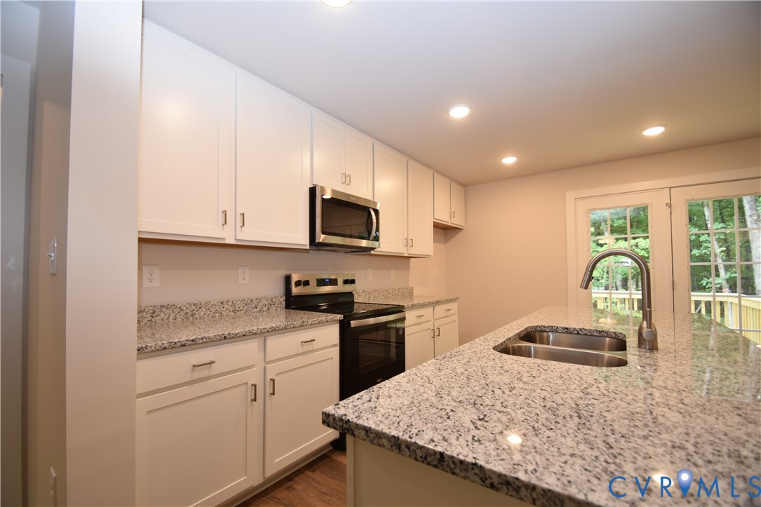 Kitchen featuring white shaker-style cabinetry, stone-finish countertops, stainless steel appliances, a center island with an undermount dual-basin sink, and recessed lighting Kitchen featuring white shaker-style cabinetry, stone-finish countertops, stainless steel appliances, a center island with an undermount dual-basin sink, and recessed lighting