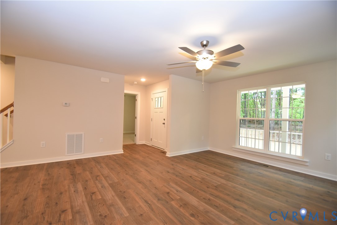Living area featuring wood-finish flooring, a multi-blade ceiling fan with integrated lighting, and a large grid-pattern window Living area featuring wood-finish flooring, a multi-blade ceiling fan with integrated lighting, and a large grid-pattern window