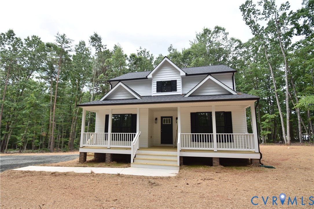 Two-story residence featuring a covered front porch with white railing, horizontal siding, black exterior shutters, and multiple dormers