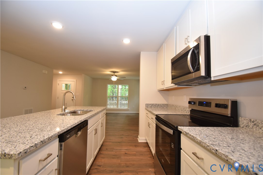 Kitchen featuring white shaker-style cabinetry, stone-surface countertops, stainless steel appliances, recessed lighting, and wood-finish flooring Kitchen featuring white shaker-style cabinetry, stone-surface countertops, stainless steel appliances, recessed lighting, and wood-finish flooring