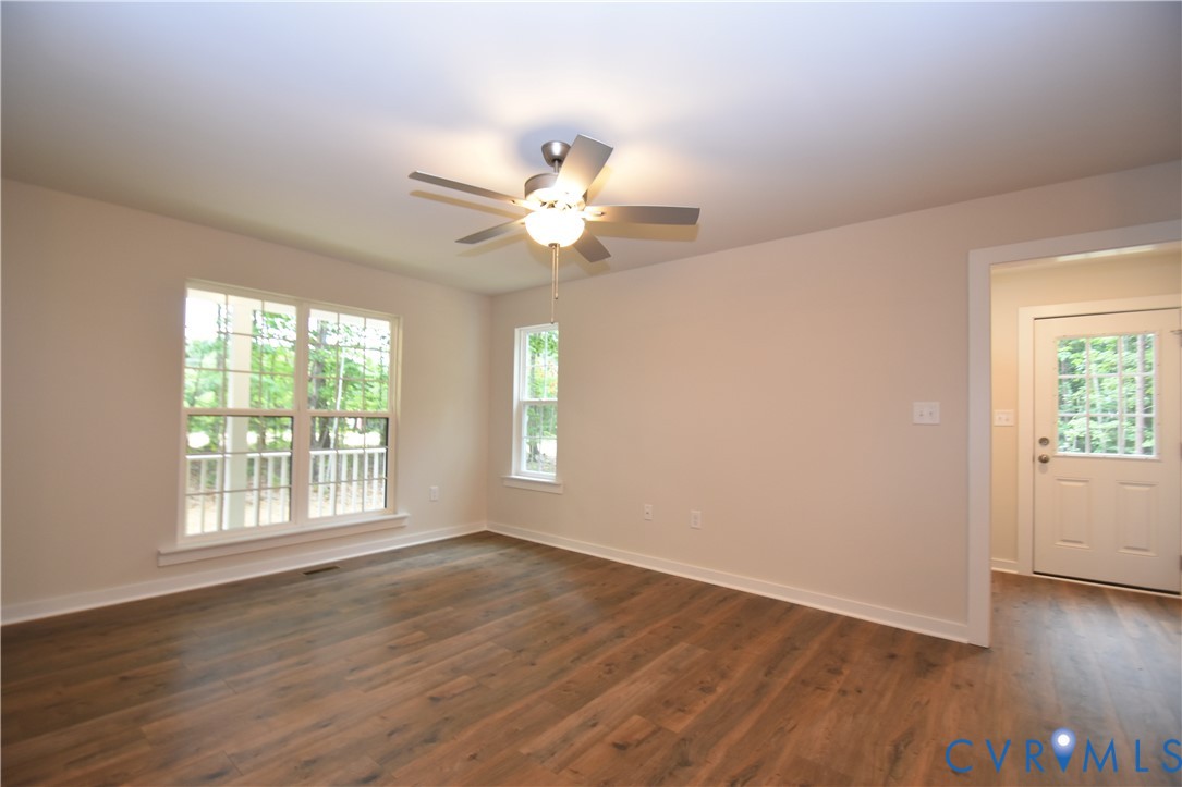 Interior space featuring wood-finish flooring, a multi-blade ceiling fan with integrated lighting, dual-pane windows, and a glass-paneled exterior door Interior space featuring wood-finish flooring, a multi-blade ceiling fan with integrated lighting, dual-pane windows, and a glass-paneled exterior door