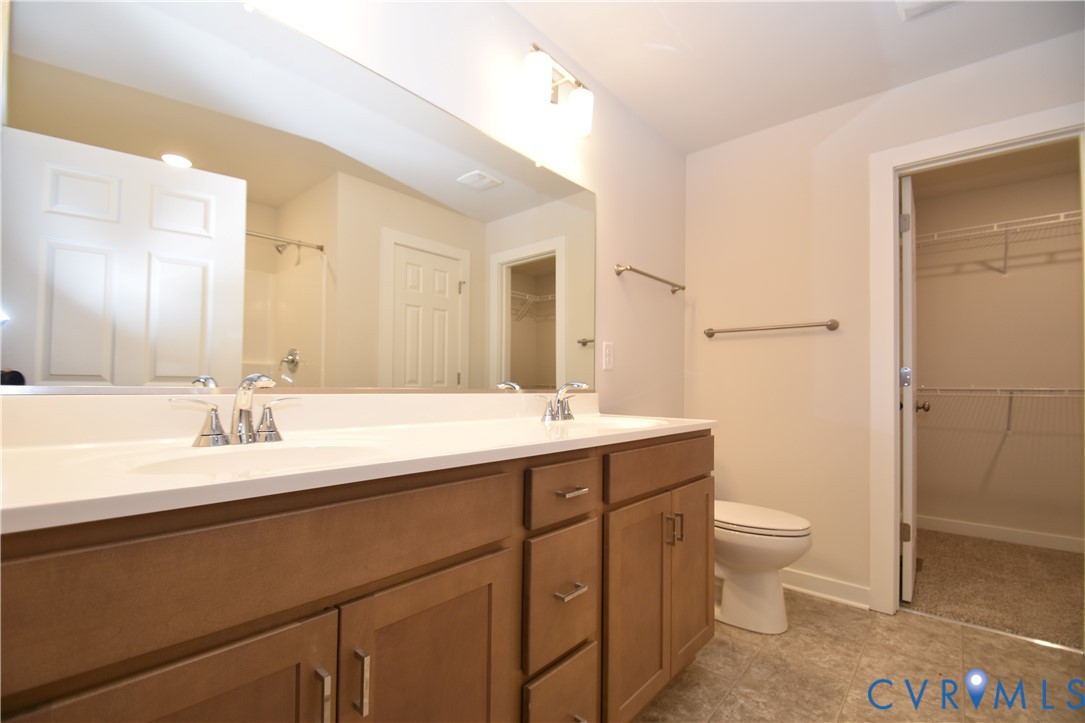 Dual-sink vanity with a solid-surface countertop, wood cabinetry, wall-to-wall mirror, and walk-in closet
