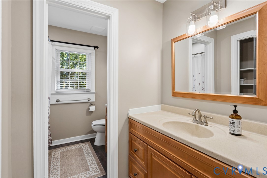 Bathroom featuring a vanity with natural wood-tone cabinetry, solid surface countertop with integrated basin, three-light wall-mounted fixture, and a large wood-framed mirror
