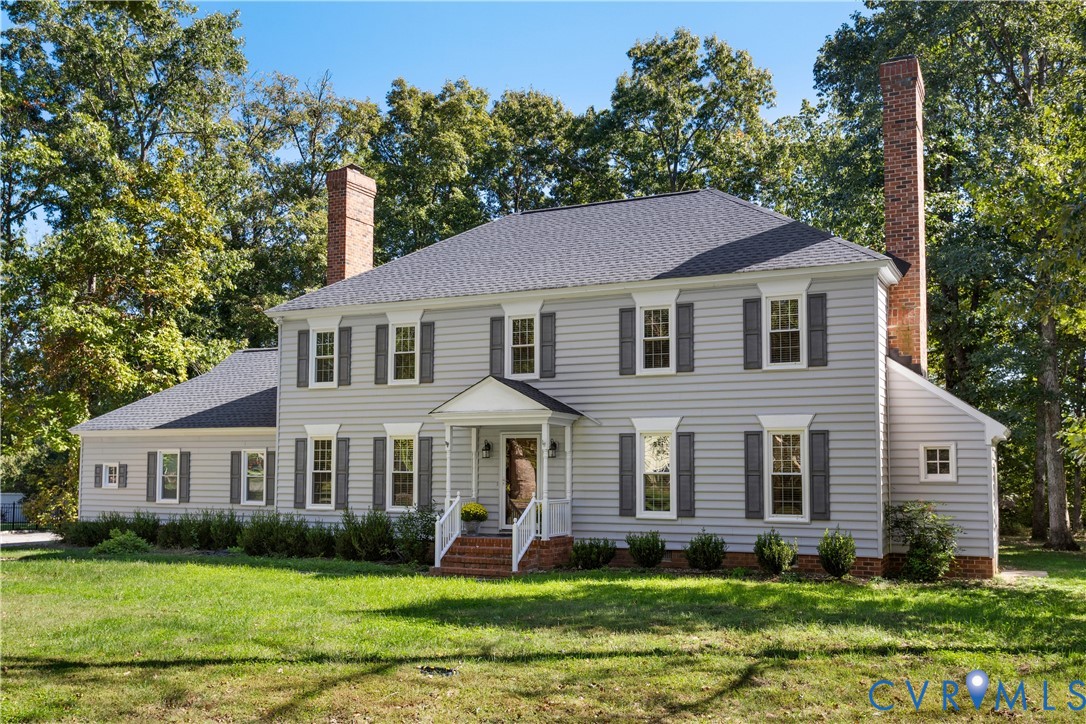 Two-story exterior featuring horizontal siding, dual brick chimneys, a covered front portico, and shutter-framed windows