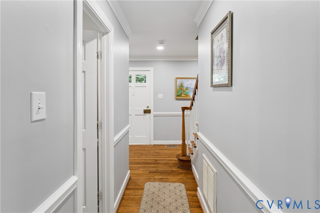 Entryway featuring wood-finish flooring, white door with glass panels, chair rail molding, and a staircase with a wooden handrail