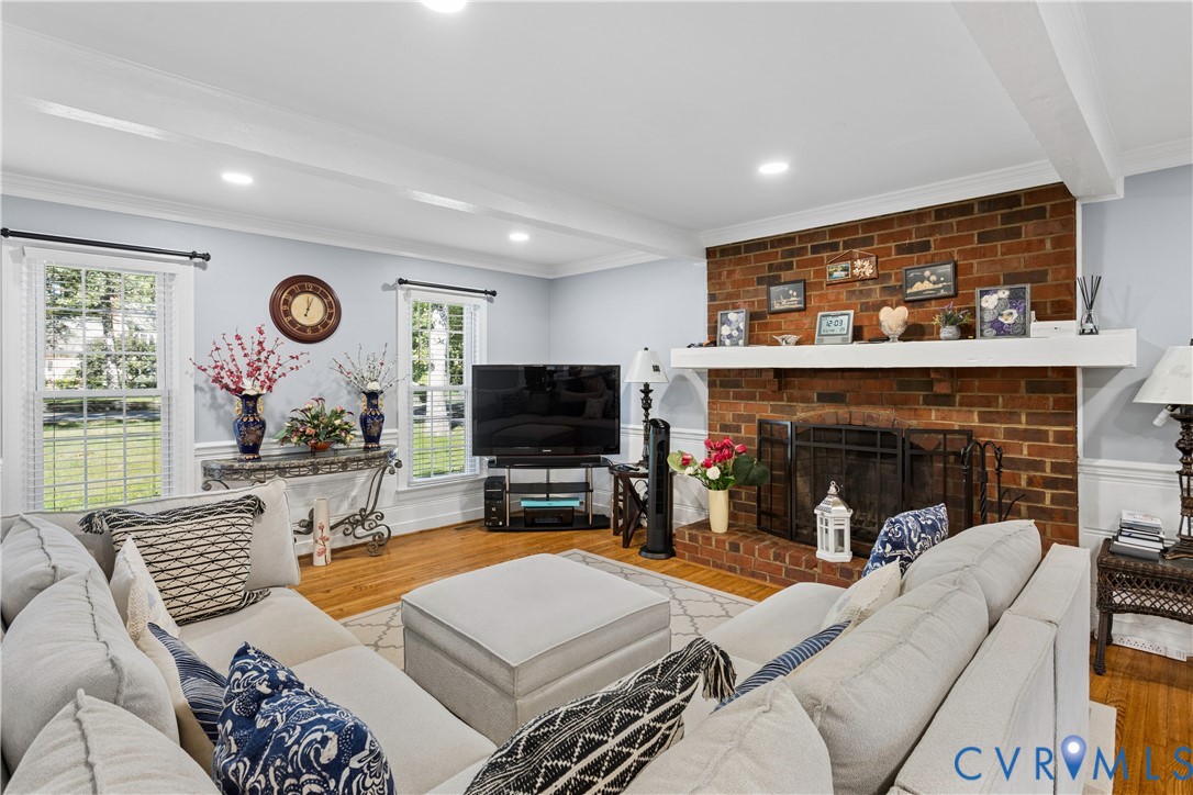 Living area featuring exposed ceiling beams, hardwood flooring, brick fireplace with a mantel, and recessed lighting