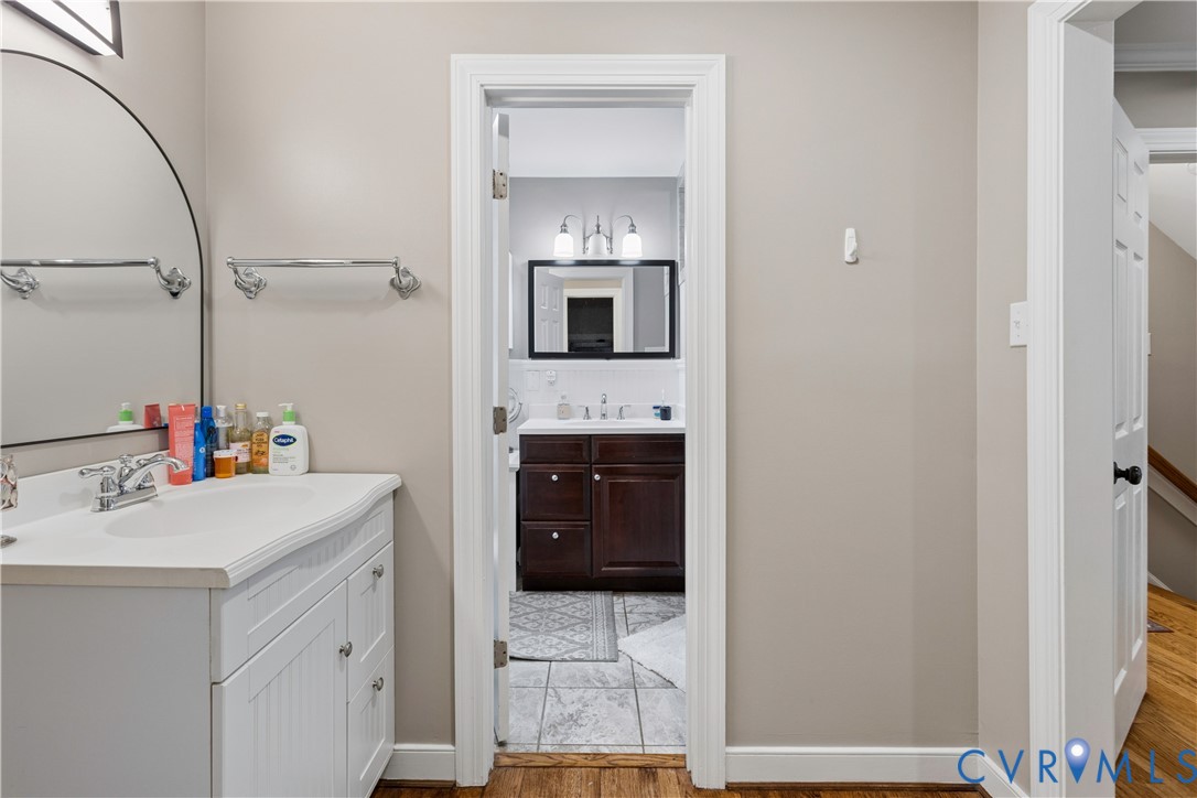 White vanity with a molded sink, polished chrome faucet, arched wall mirror, and secondary bathroom featuring a dark wood cabinet, multi-light fixture, and tiled flooring