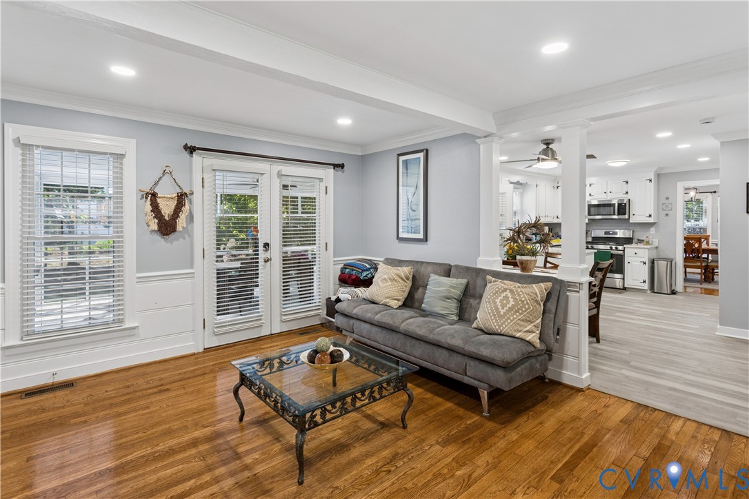 Hardwood flooring, wood-panel wainscoting, glass-paned double doors, and white-painted architectural columns