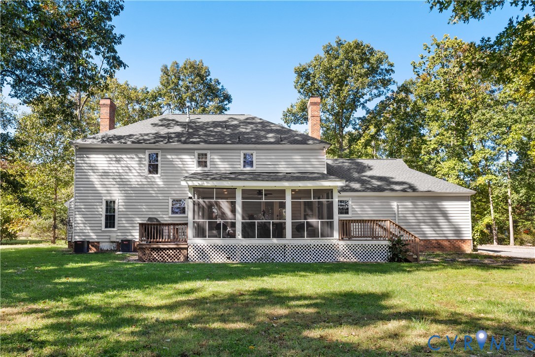 Rear exterior featuring horizontal lap siding, two masonry chimneys, a large screened-in porch, an attached wooden deck, and a expansive lawn surrounded by mature trees