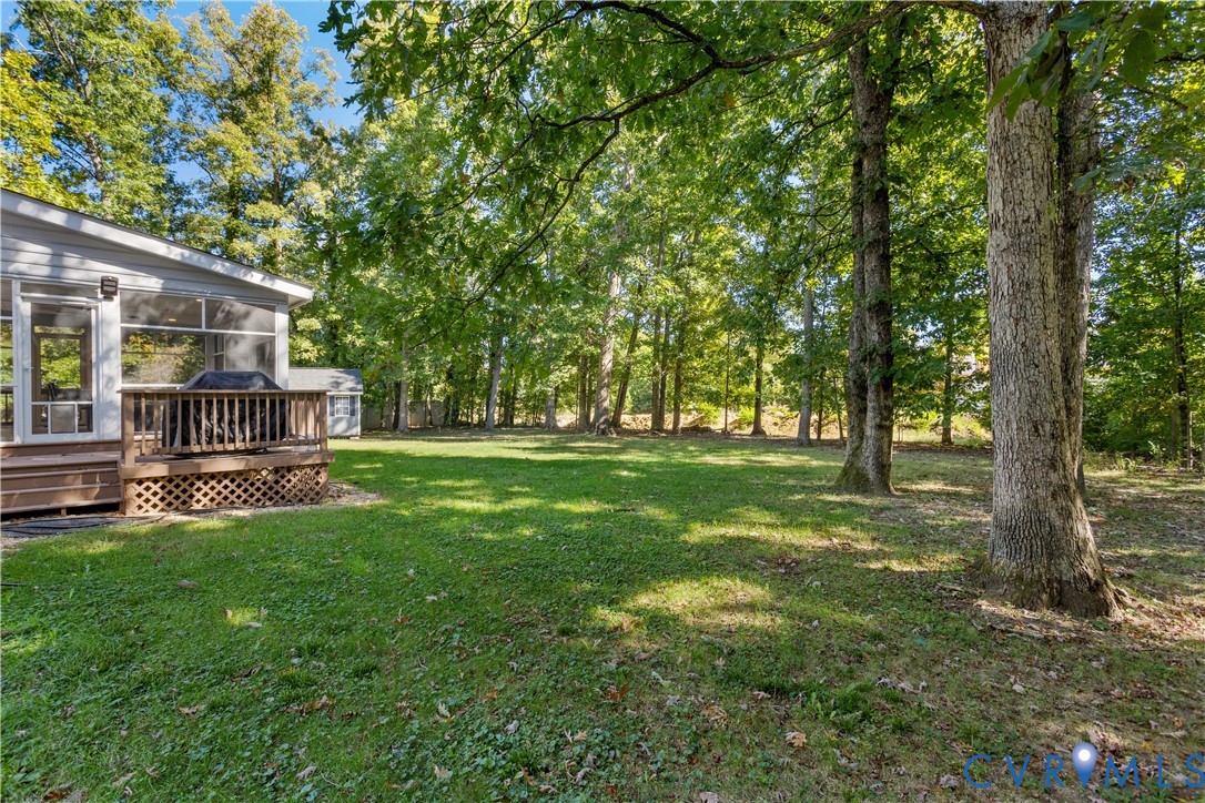 Spacious backyard featuring a wood deck with lattice skirting and mature trees