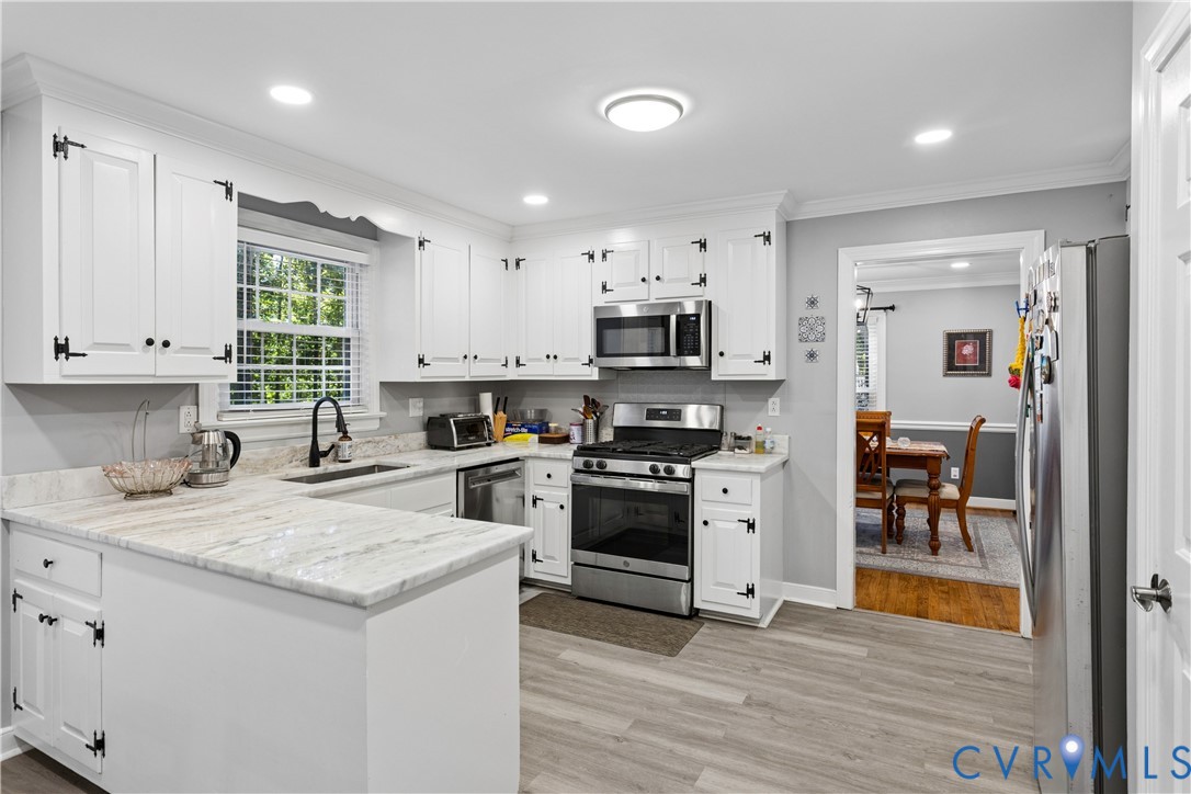 Kitchen featuring white cabinetry with matte black hardware, stone-finish countertops, stainless steel appliances, and wood-finish flooring