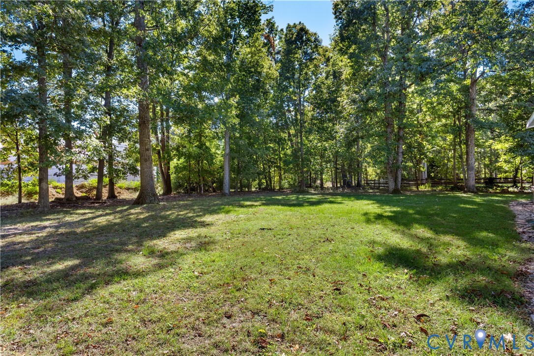 Expansive backyard featuring a level grass lawn, mature trees, and wooden perimeter fencing