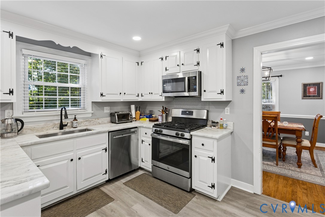 Kitchen featuring white cabinetry with matte black hardware, stone-finish countertops, stainless steel appliances, and wood-finish flooring