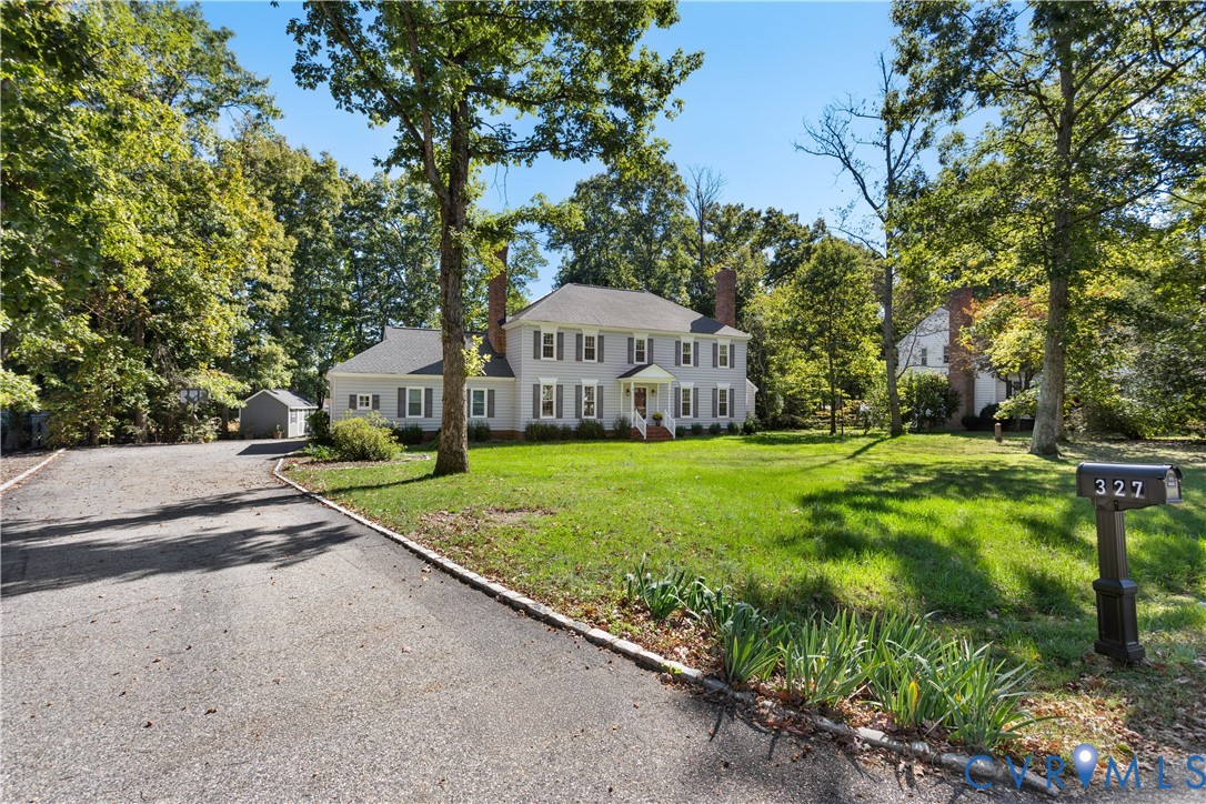 Two-story Colonial exterior featuring gray siding, symmetrically placed windows with shutters, twin brick chimneys, and an attached gravel driveway