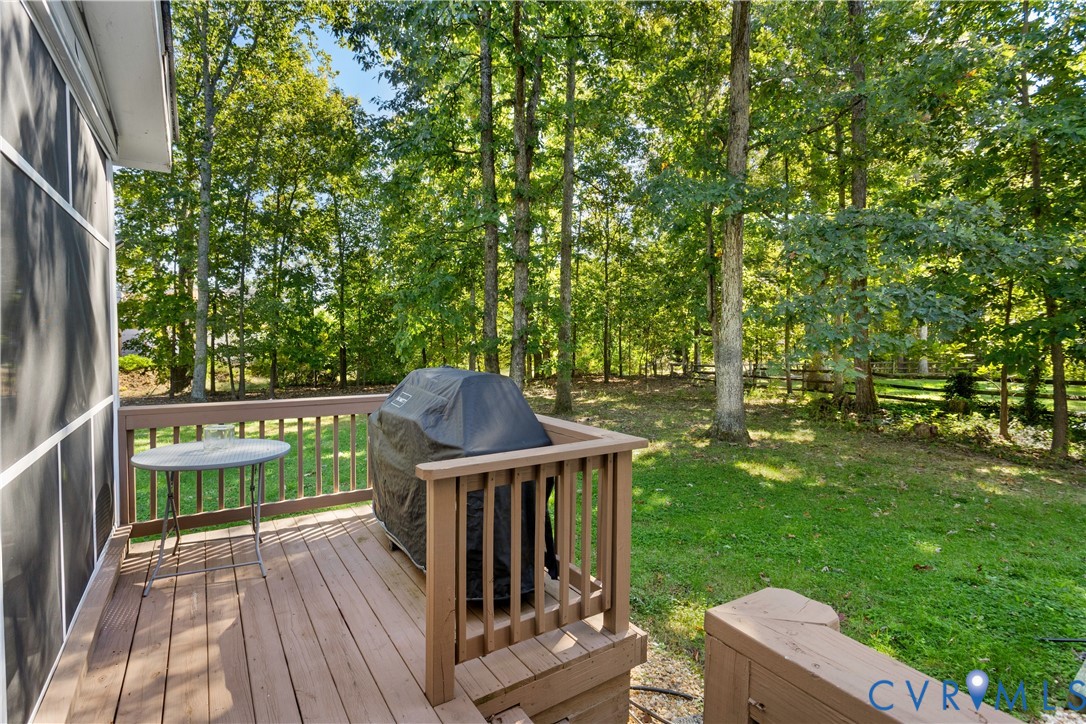 Elevated wood-finished deck featuring a wooden balustrade, overlooking a private backyard with mature trees and a split-rail fence