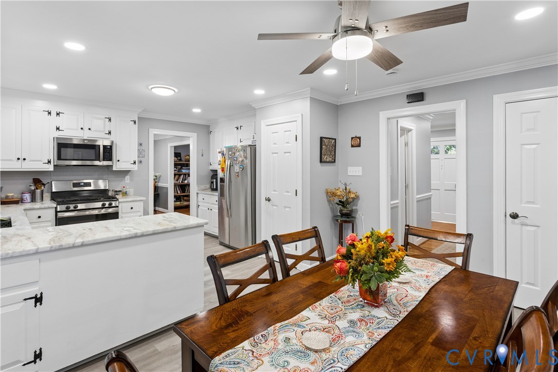 Kitchen featuring white shaker-style cabinetry, stone-surface countertops, stainless steel appliances, wood-finish flooring, and a ceiling-mounted light fixture with a fan