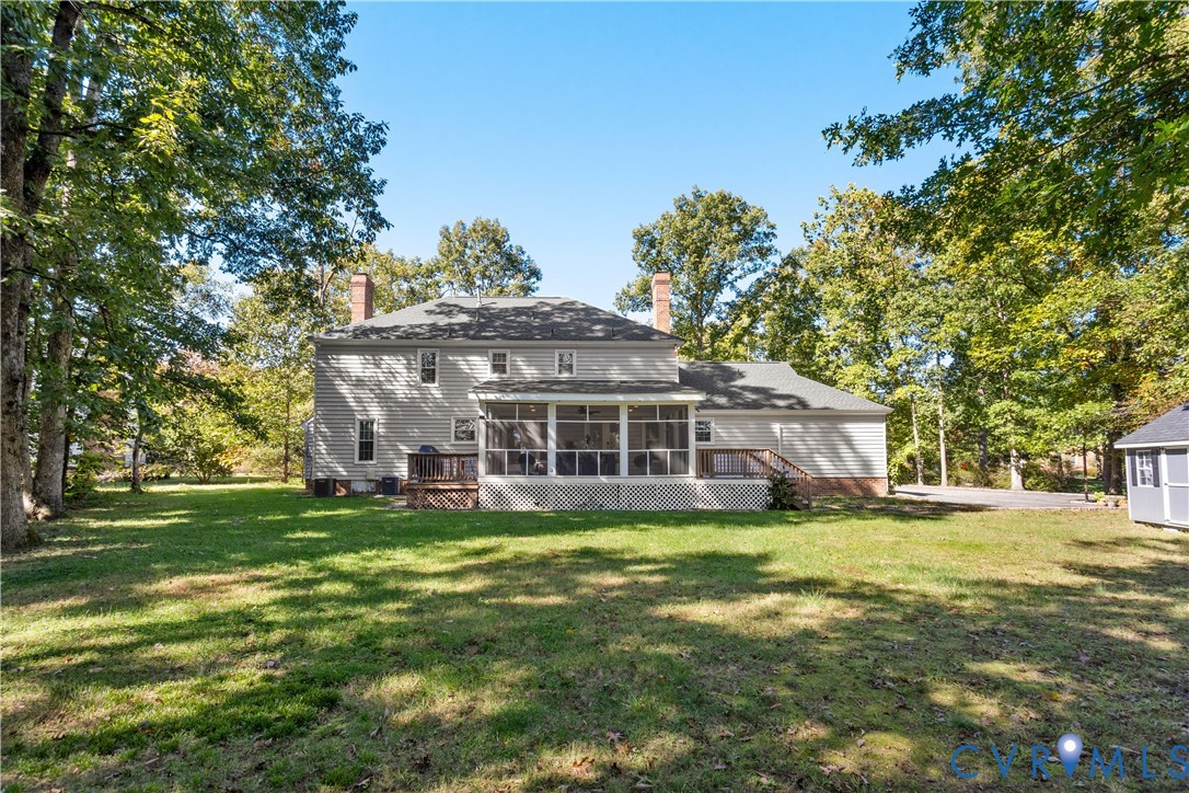 Rear exterior featuring horizontal lap siding, a screened-in porch, dual brick chimneys, an open wood deck, and a expansive lawn surrounded by mature trees