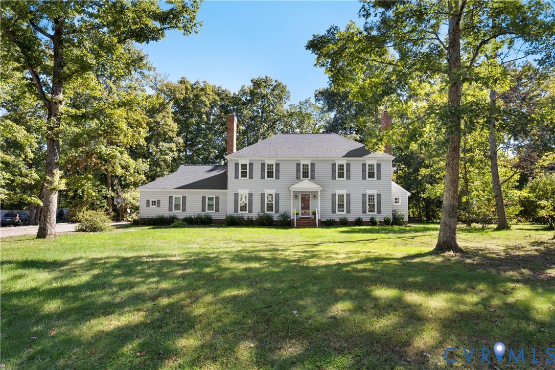 Two-story traditional exterior featuring light-toned horizontal siding, a symmetrical faade with multi-pane windows, a covered front entryway, two brick chimneys, and a sprawling lot with mature trees
