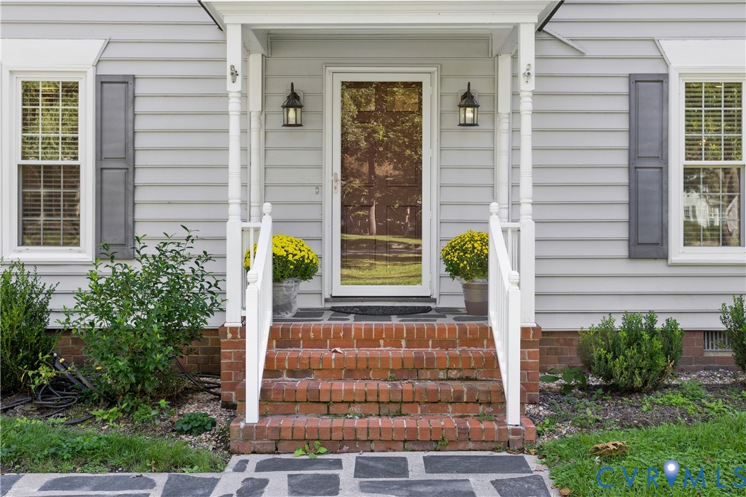Front entrance featuring horizontal siding, shutters, brick steps with white railings, and wall-mounted lanterns
